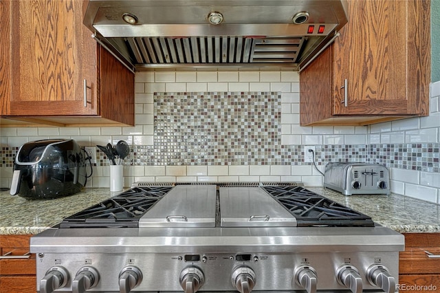 kitchen featuring stainless steel range oven, range hood, light stone counters, and brown cabinets