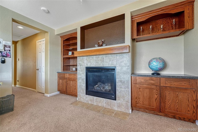 living area featuring light carpet, a tiled fireplace, baseboards, and built in features