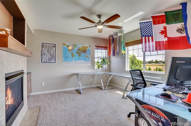 office featuring a ceiling fan, baseboards, light carpet, and a tiled fireplace