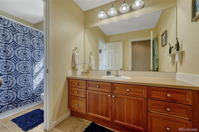 bathroom featuring a textured wall, toilet, vanity, baseboards, and tile patterned floors