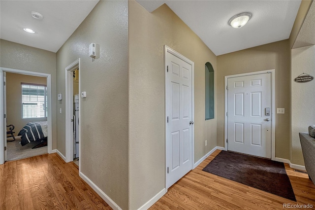 hallway featuring light wood-type flooring, baseboards, and arched walkways