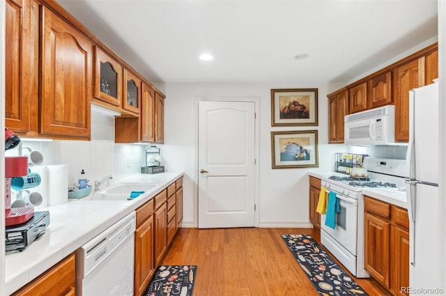 kitchen with glass insert cabinets, tile counters, light wood-style flooring, brown cabinets, and white appliances