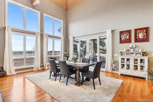 dining area with french doors, baseboards, light wood-style floors, and a towering ceiling