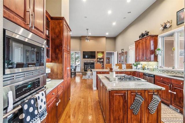 kitchen with light wood-type flooring, a peninsula, appliances with stainless steel finishes, a glass covered fireplace, and tasteful backsplash