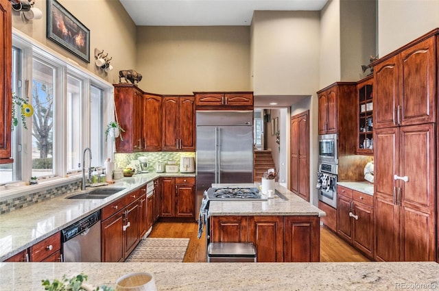 kitchen featuring built in appliances, light stone counters, decorative backsplash, a towering ceiling, and a sink