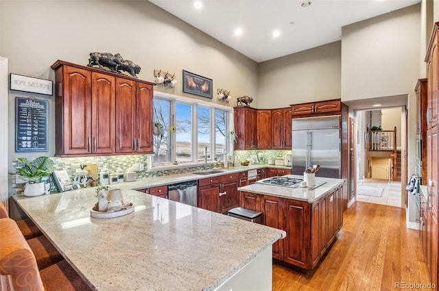 kitchen with light stone countertops, a peninsula, stainless steel appliances, decorative backsplash, and a towering ceiling