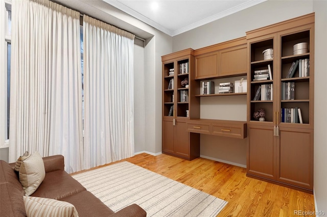 office space with crown molding, built in desk, and light wood-type flooring