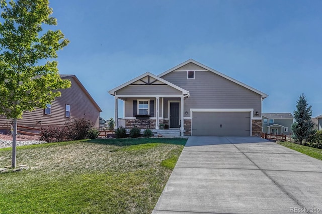 craftsman-style home with covered porch, concrete driveway, an attached garage, a front yard, and stone siding