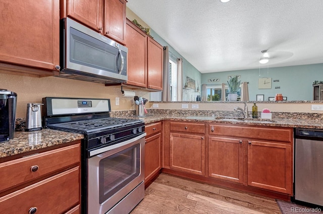 kitchen with light wood-type flooring, a textured ceiling, stainless steel appliances, sink, and dark stone countertops