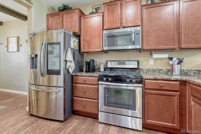 kitchen with light hardwood / wood-style floors, light stone counters, and stainless steel appliances