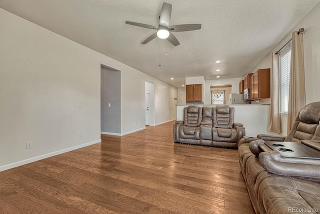 living room featuring ceiling fan, a textured ceiling, baseboards, and wood finished floors