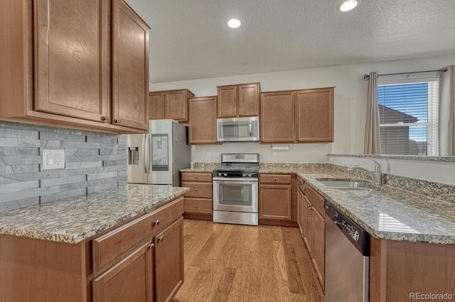 kitchen featuring appliances with stainless steel finishes, light wood-style floors, brown cabinetry, and a sink