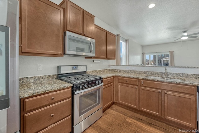 kitchen featuring light stone counters, appliances with stainless steel finishes, a sink, a textured ceiling, and wood finished floors