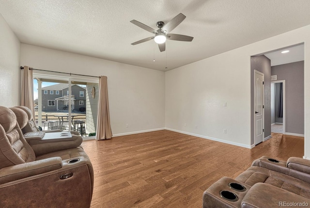 living room with ceiling fan, a textured ceiling, baseboards, and wood finished floors