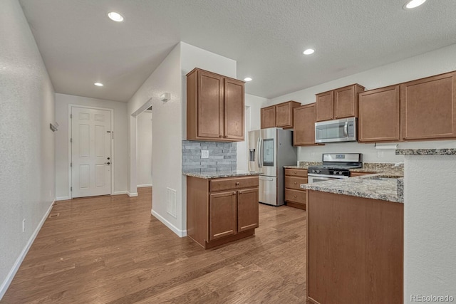 kitchen featuring stainless steel appliances, light wood-style floors, baseboards, and light stone countertops