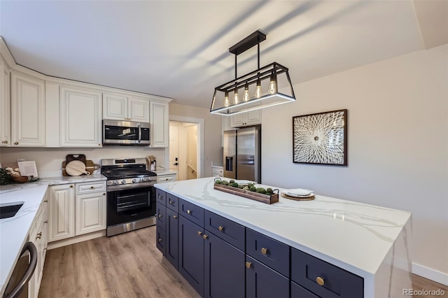 kitchen with hanging light fixtures, a kitchen island, stainless steel appliances, light hardwood / wood-style floors, and white cabinets