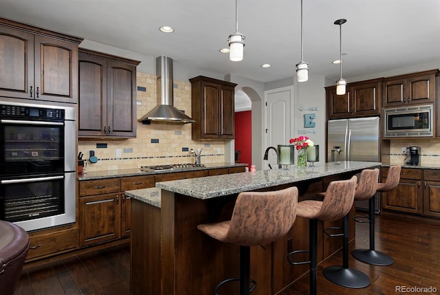 1315 W 141st Cir, Westminster, CO 80023 - kitchen with stainless steel appliances, wall chimney range hood, arched walkways, decorative backsplash, and dark wood-style flooring