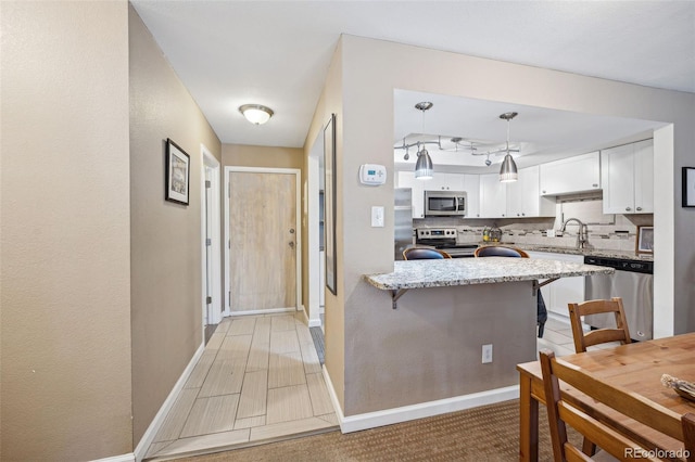 kitchen with white cabinetry, hanging light fixtures, stainless steel appliances, a kitchen breakfast bar, and kitchen peninsula