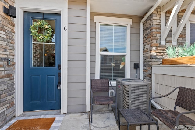 property entrance featuring stone siding, central AC unit, a porch, and brick siding