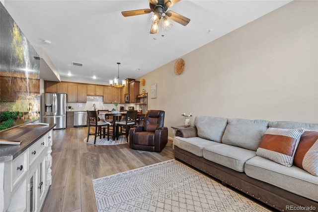 living area featuring ceiling fan with notable chandelier, visible vents, and light wood-style floors