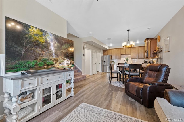 living area featuring stairs, baseboards, a chandelier, and light wood-style floors