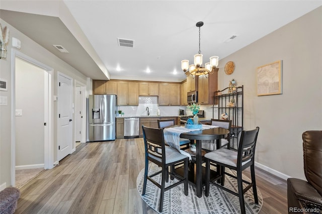 dining area featuring a chandelier, light wood-type flooring, visible vents, and baseboards