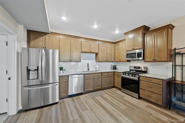 kitchen with stainless steel appliances, recessed lighting, light wood-style flooring, a sink, and light stone countertops