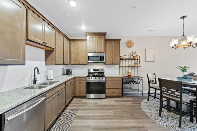 kitchen with backsplash, light wood-style flooring, appliances with stainless steel finishes, a sink, and light stone countertops