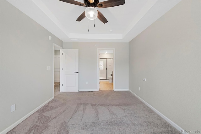 unfurnished bedroom with a ceiling fan, a raised ceiling, baseboards, carpet, and ensuite bath