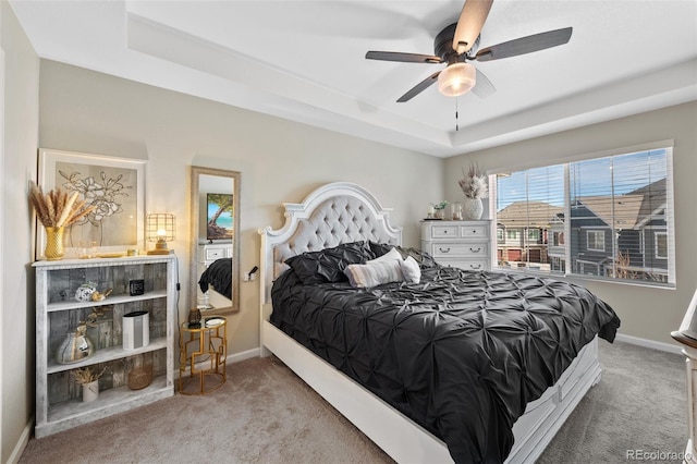 carpeted bedroom with a tray ceiling, ceiling fan, and baseboards