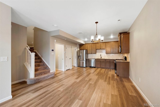 kitchen featuring light countertops, tasteful backsplash, light wood finished floors, appliances with stainless steel finishes, and a notable chandelier