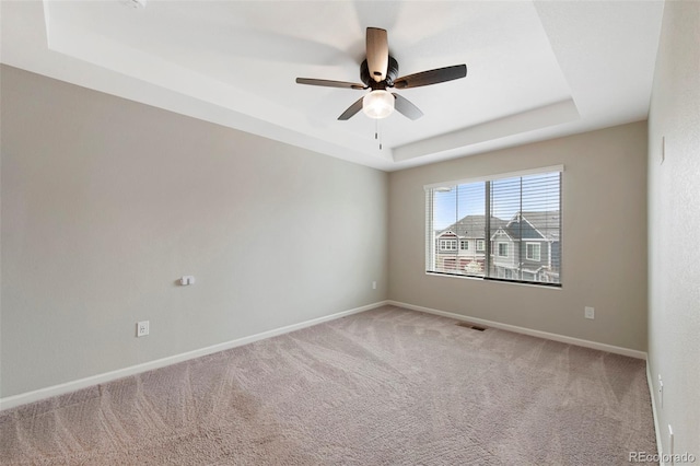 empty room featuring a raised ceiling, ceiling fan, light carpet, and visible vents