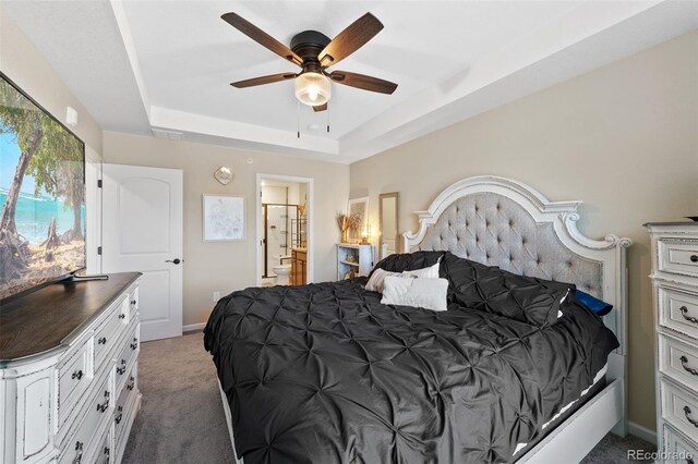 carpeted bedroom with baseboards, ceiling fan, a tray ceiling, and ensuite bath