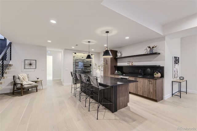 kitchen with pendant lighting, a kitchen bar, dark brown cabinets, light hardwood / wood-style floors, and a kitchen island