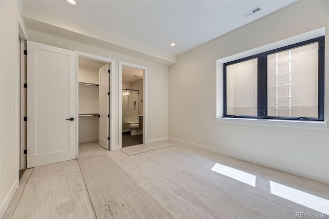 unfurnished bedroom featuring a walk in closet, ensuite bath, a closet, and light carpet