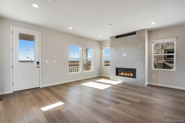 unfurnished living room featuring a tiled fireplace, light wood-type flooring, baseboards, and recessed lighting