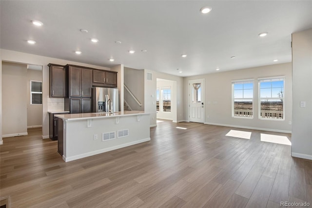 kitchen featuring open floor plan, light countertops, dark brown cabinets, stainless steel fridge, and a center island with sink