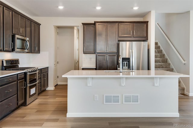 kitchen with stainless steel appliances, light countertops, a kitchen island with sink, and a kitchen breakfast bar