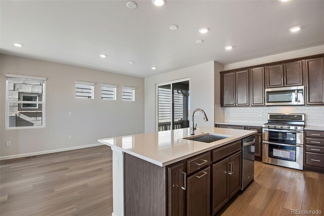 kitchen featuring light countertops, appliances with stainless steel finishes, a sink, and a center island with sink