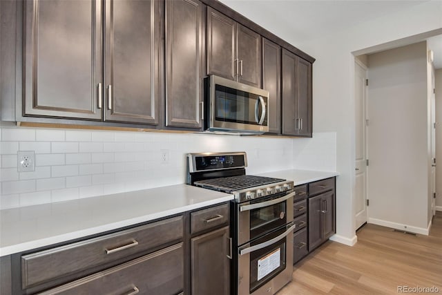 kitchen with tasteful backsplash, stainless steel appliances, dark brown cabinets, light countertops, and light wood-style floors