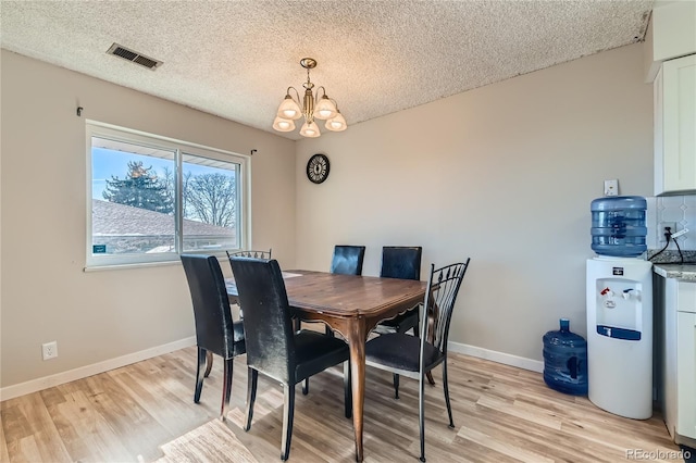 dining space featuring a textured ceiling, an inviting chandelier, and light hardwood / wood-style flooring