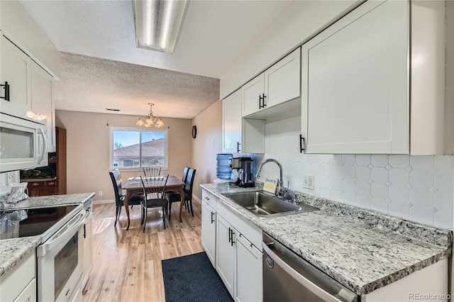 kitchen with white cabinetry, sink, pendant lighting, and white appliances