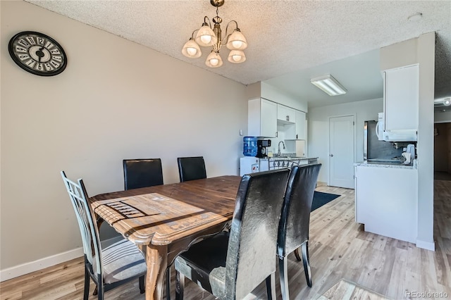 dining space featuring sink, a textured ceiling, light hardwood / wood-style flooring, and a chandelier