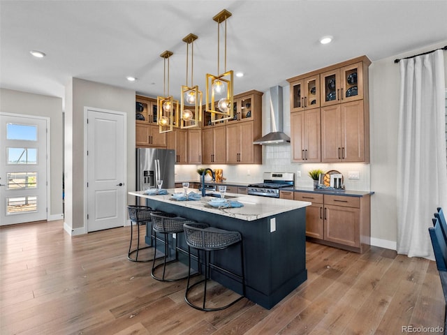 1787 W 166th Ave, Broomfield, CO 80023 - kitchen featuring wall chimney range hood, stainless steel appliances, a breakfast bar, a center island with sink, and light wood-type flooring