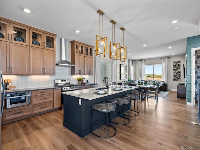 1787 W 166th Ave, Broomfield, CO 80023 - kitchen with wall chimney range hood, appliances with stainless steel finishes, wood finished floors, an island with sink, and decorative backsplash