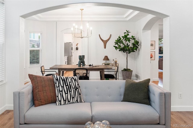 living room with light hardwood / wood-style floors, a raised ceiling, and a chandelier