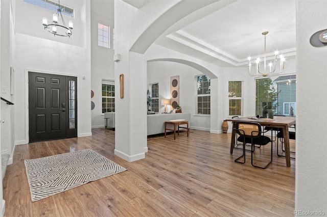 foyer with an inviting chandelier, a raised ceiling, and light hardwood / wood-style flooring