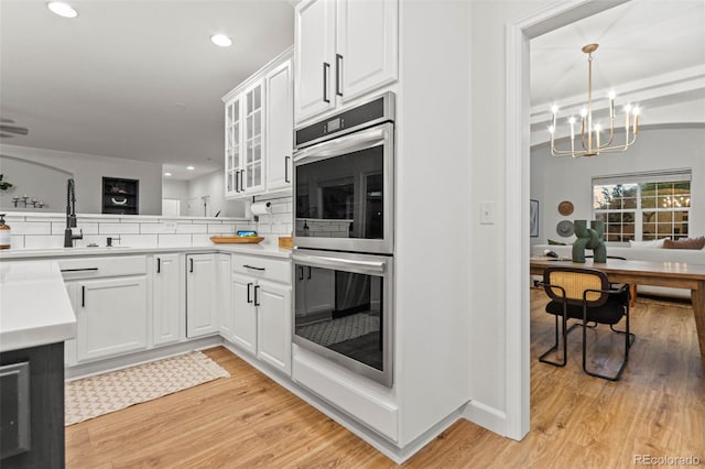 kitchen featuring light wood-type flooring, double oven, an inviting chandelier, white cabinetry, and hanging light fixtures