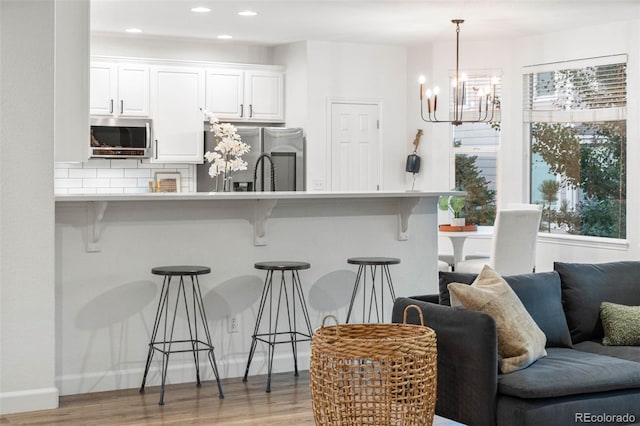 kitchen featuring white cabinets, appliances with stainless steel finishes, a kitchen bar, and hanging light fixtures