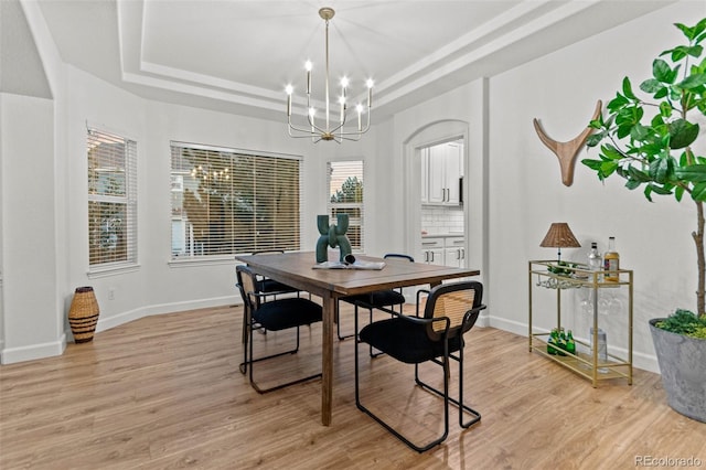 dining area with light hardwood / wood-style floors, a raised ceiling, and a chandelier